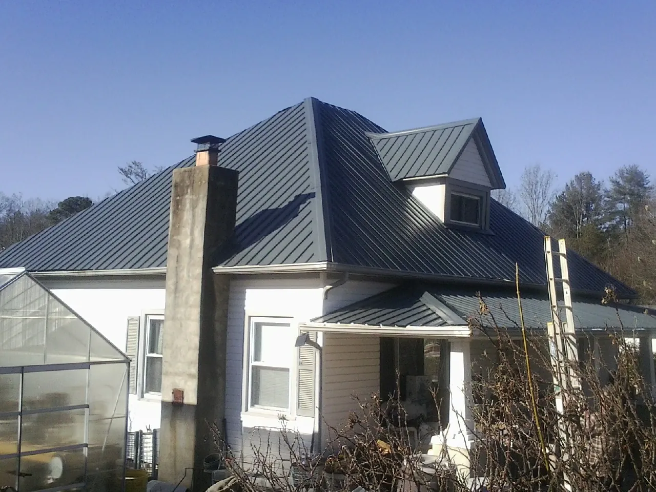 Dark blue standing seam metal roof on a white farmhouse with dormer — Slate & Tile Roof Repair by Roofing Brothers in Camino