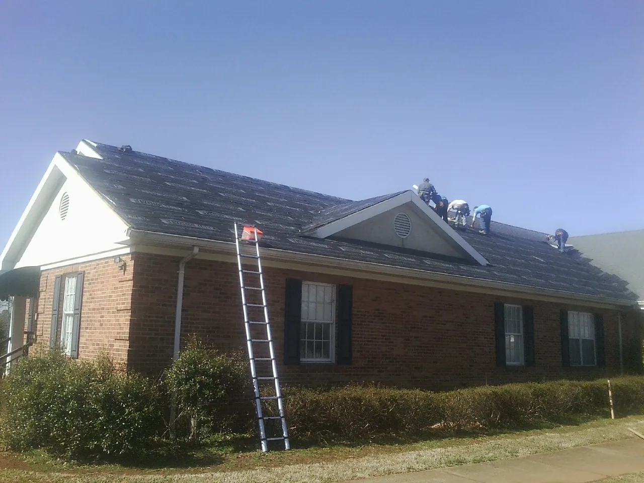 Crew tearing shingles off a brick ranch roof with a ladder set — Emergency Roof Repair work by our crew in Camino