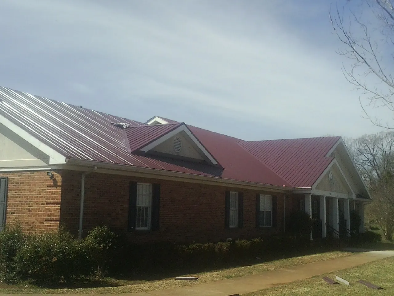 Red metal roof with gabled entries on a long brick building, from a Hail Damage Roof Repair job in Camino