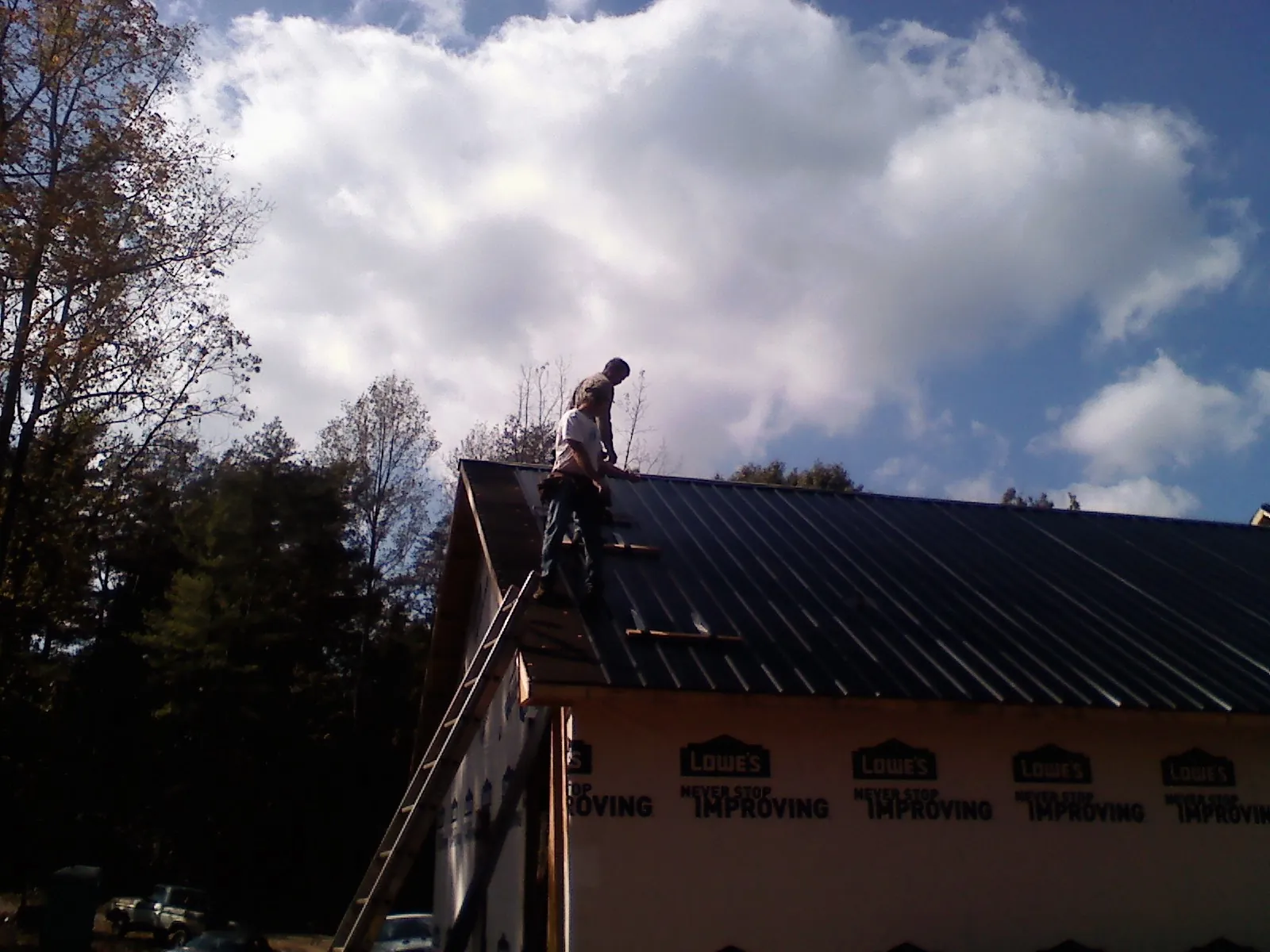 Roofer fastening dark metal panels high against a cloudy sky, from a Roof Inspection job in Camino