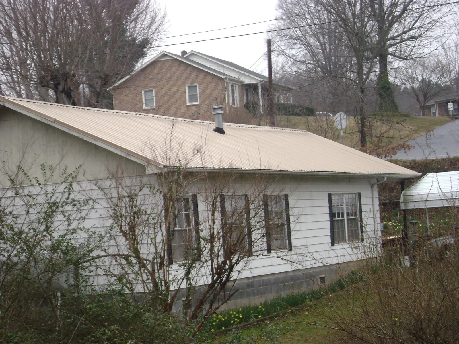 Tan metal roof on a white sided house set into a hillside — Commercial Roofing by Roofing Brothers in Camino